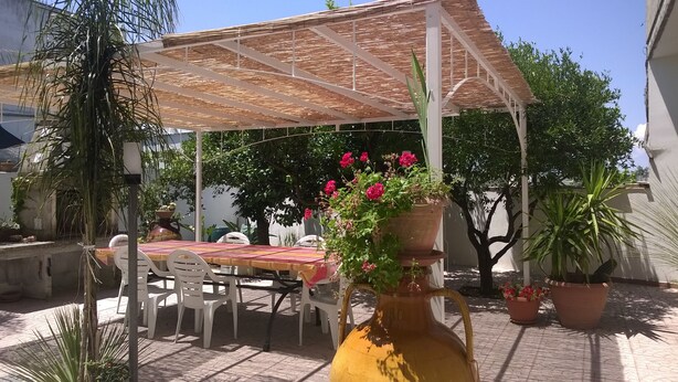An outdoor patio with a table and chairs, a pergola, and potted plants. - Arcona (Carpignano Salentino)