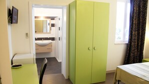 A room with a green wardrobe, a bed, a small table, and a bathroom visible through an open door. - Arcona (Carpignano Salentino)