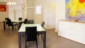 A dining area with a glass-top table and black chairs, a white cabinet with drawers, and a colorful abstract painting on the wall. - Arcona (Carpignano Salentino)