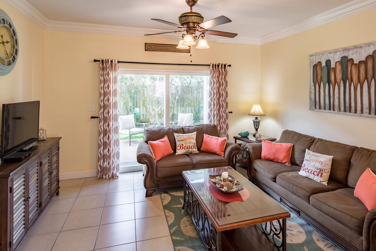 A living room with a brown sofa, a coffee table, a TV on a cabinet, and a ceiling fan.