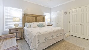 Une chambre à coucher comprenant un lit, des tables de chevet, une tête de lit en bois, un ventilateur de plafond et une armoire avec des portes.