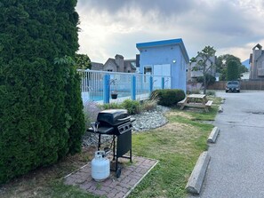 A residential area with a blue building, a barbecue grill, a gas cylinder, and a fenced pool. - Golden Sands Resort Motel (Penticton)