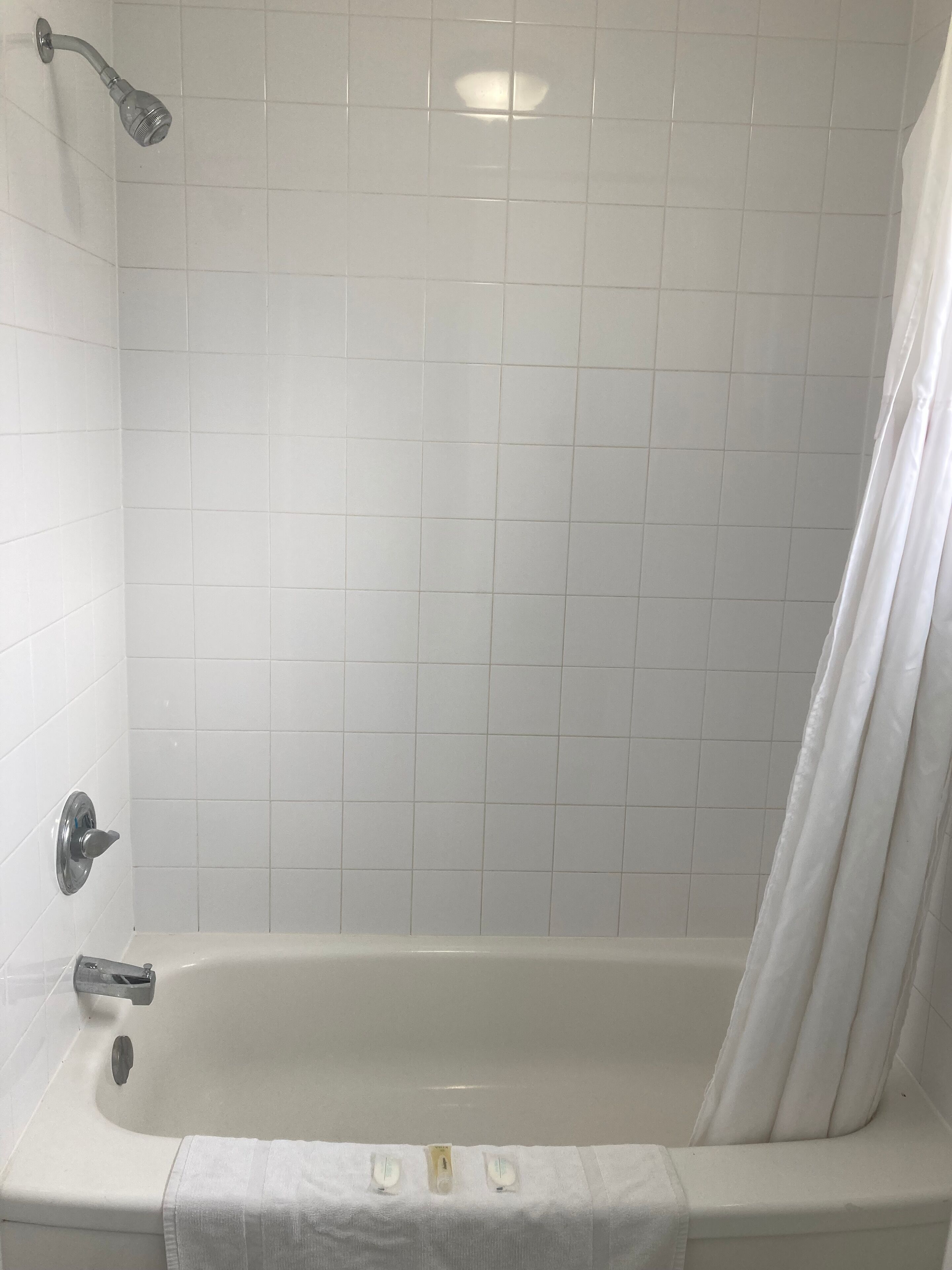 A bathroom with a bathtub, white tiled walls, a showerhead, and a curtain.