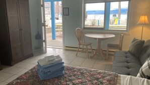 A room with a bed, a chair, a table, a view of the outdoors, and a door leading outside. - Golden Sands Resort Motel (Penticton)