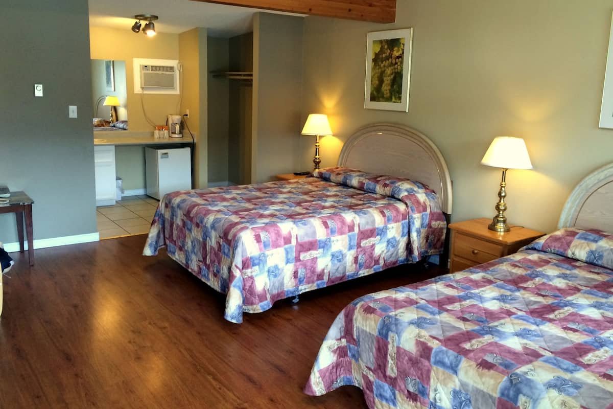 Een slaapkamer met twee bedden, een houten plafond, een kleine kitchenette en een zichtbare badkamer door een open deur.