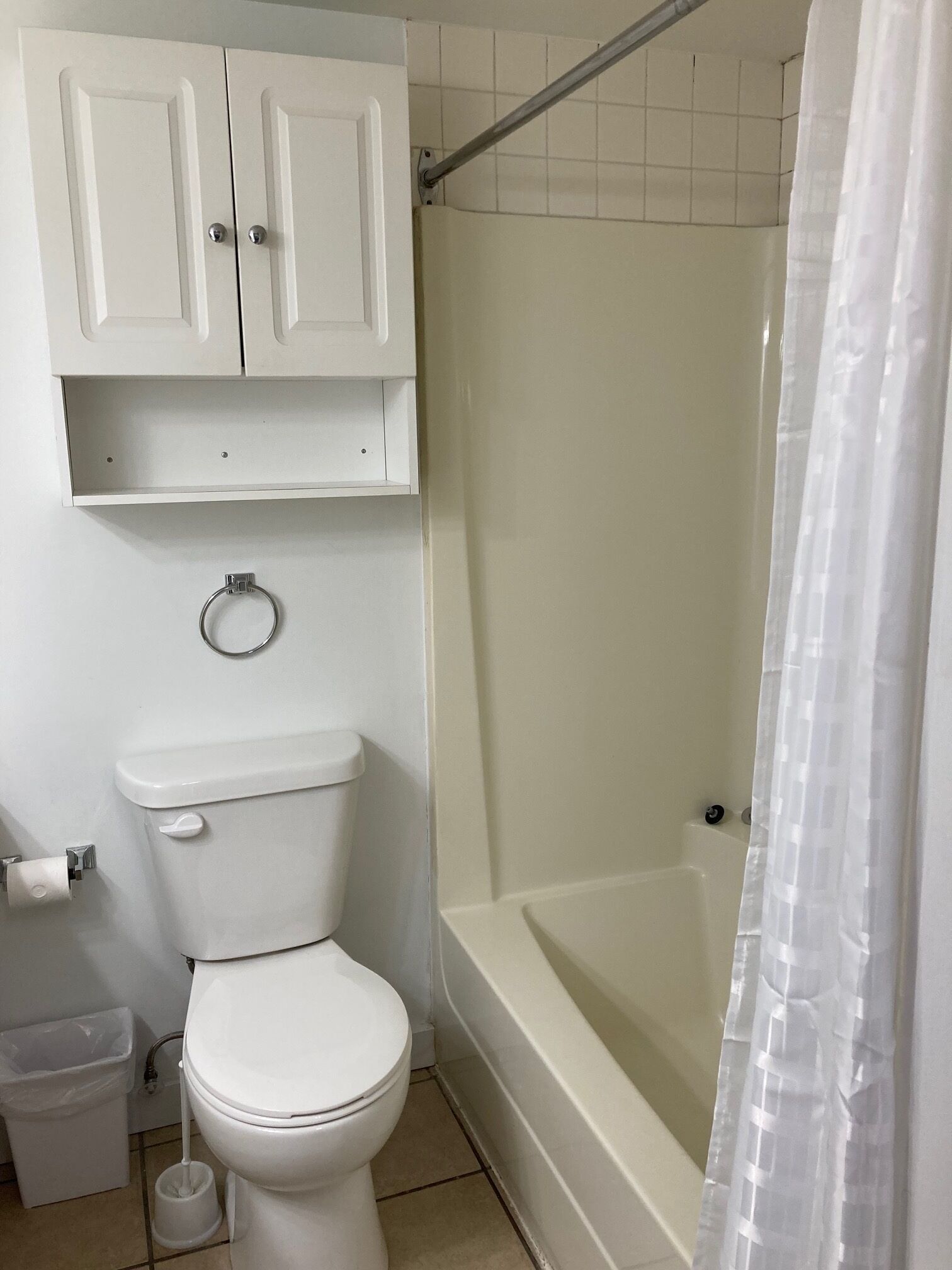 A bathroom with a toilet, a shower with a glass door, and a small cabinet above the toilet.