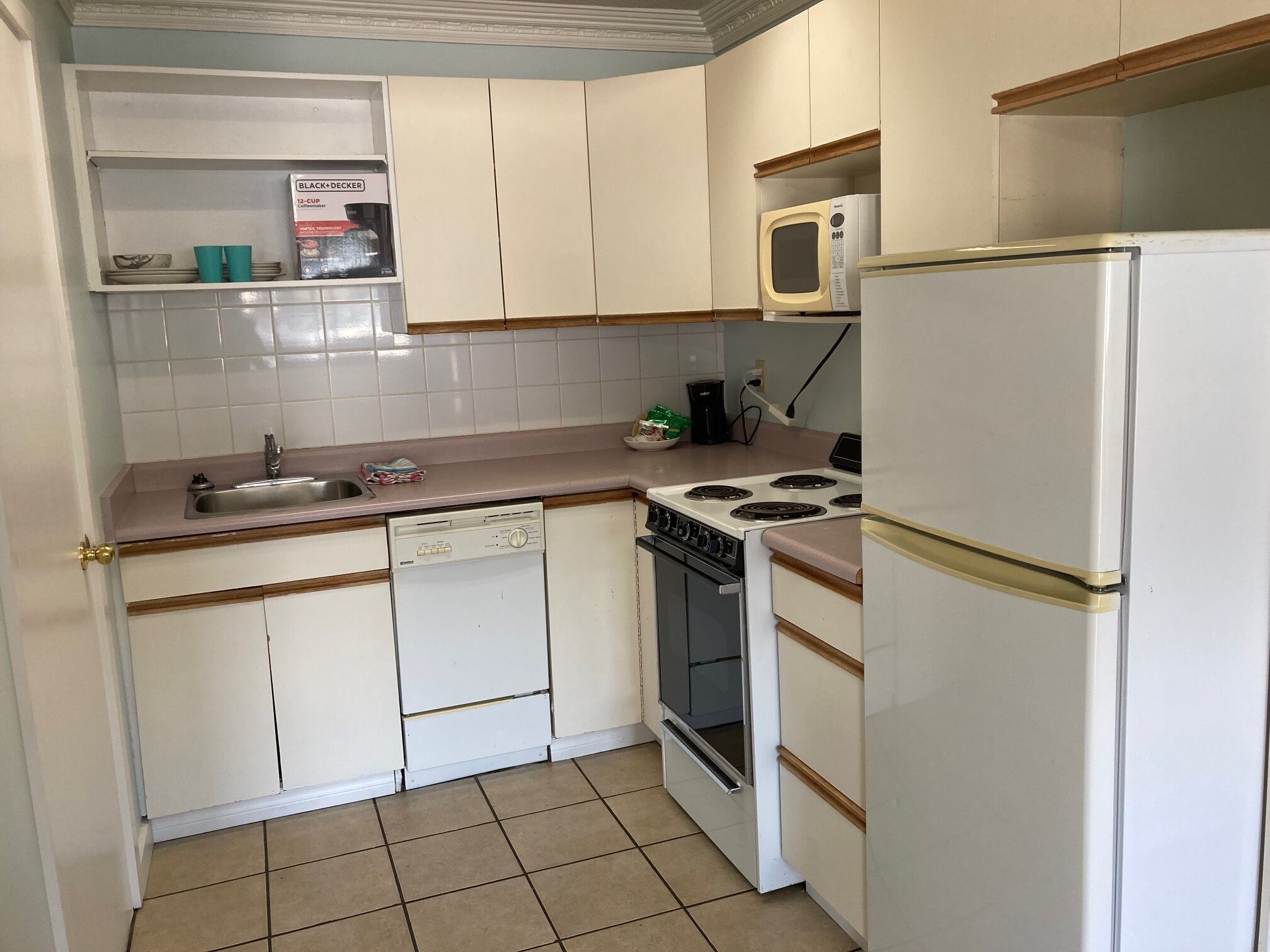 Una cocina compacta con armarios blancos, un lavabo, una estufa y un microondas.