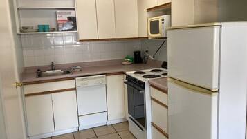 Una cocina compacta con armarios blancos, un lavabo, una estufa y un microondas.