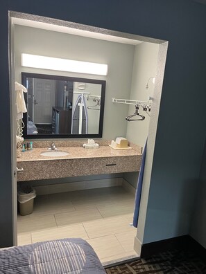 A hotel bathroom with a granite countertop sink, a mirror, a towel rack, and a shower area. - Brandon Motor Lodge (Brandon)