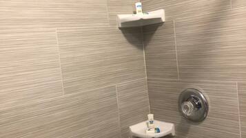 A shower area with a textured wall, a circular showerhead, and two white shelves with toiletries.