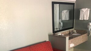 Un divano rosso in un bagno con uno specchio sopra il lavabo e un porta asciugamani a parete.
