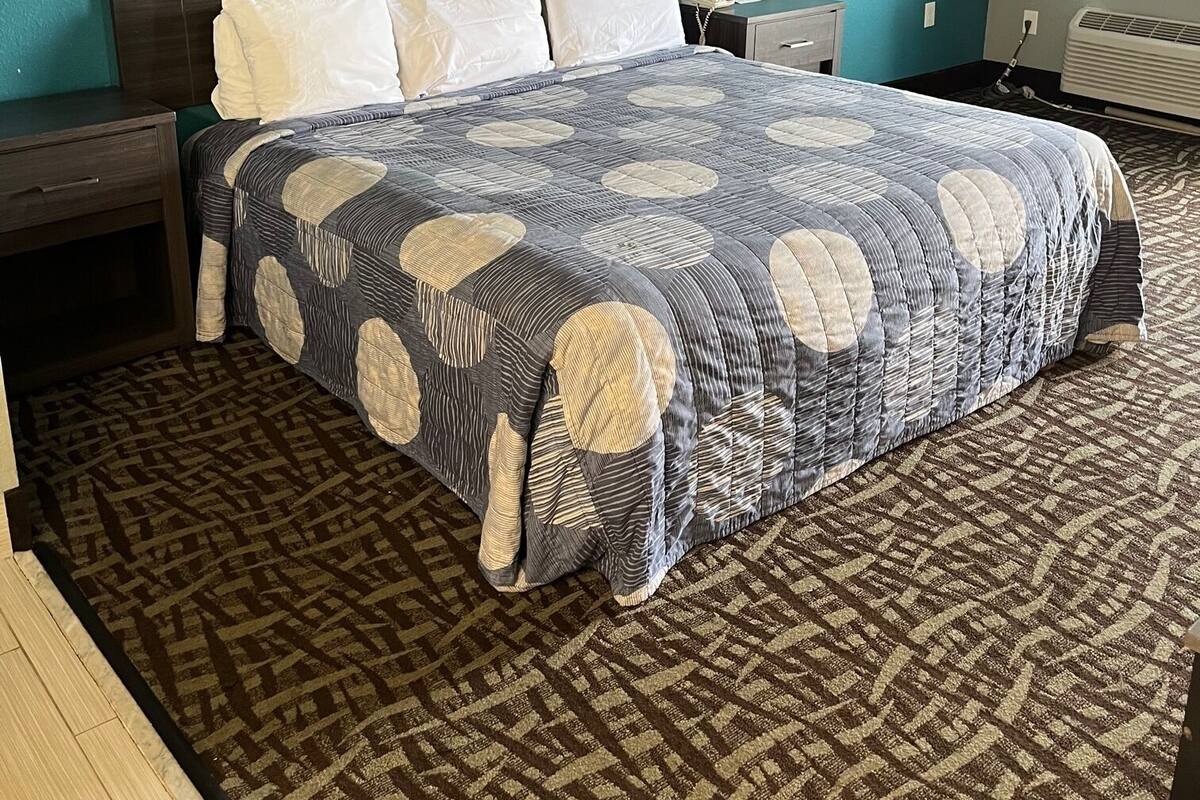 A hotel room with a large bed, a nightstand, a desk, a chair, and a window with curtains.