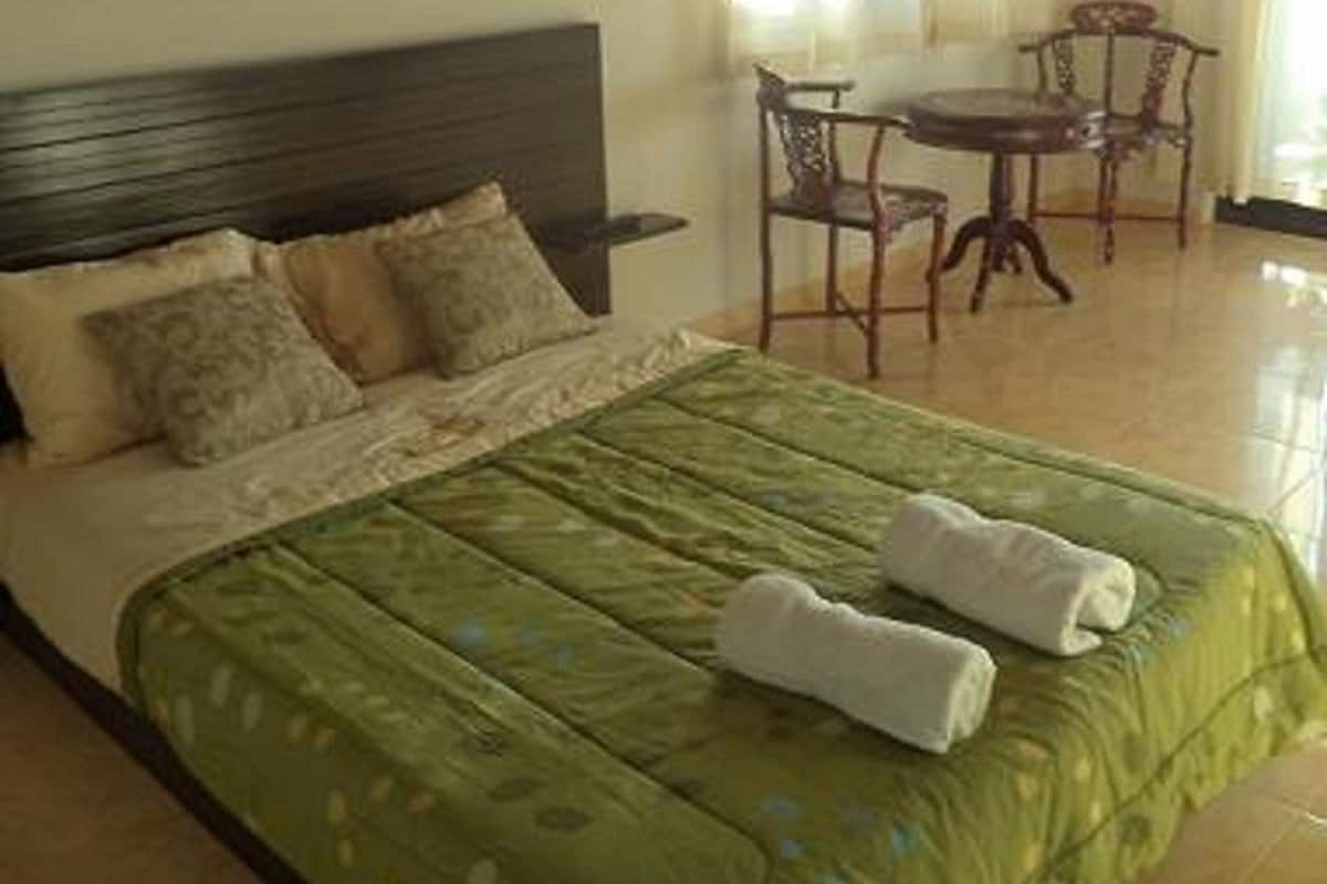 Una habitación de hotel con cama, un cuadro de flores en la pared, una mesa de comedor con sillas y una ventana con cortinas.