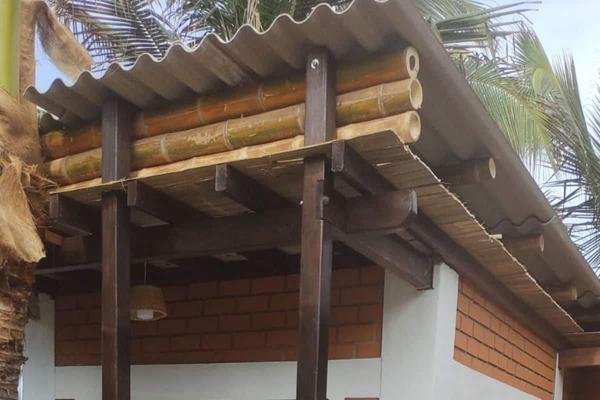 Un edificio con fachada de ladrillo, una pérgola de madera con postes de bambú y un área de entrada con tejas.