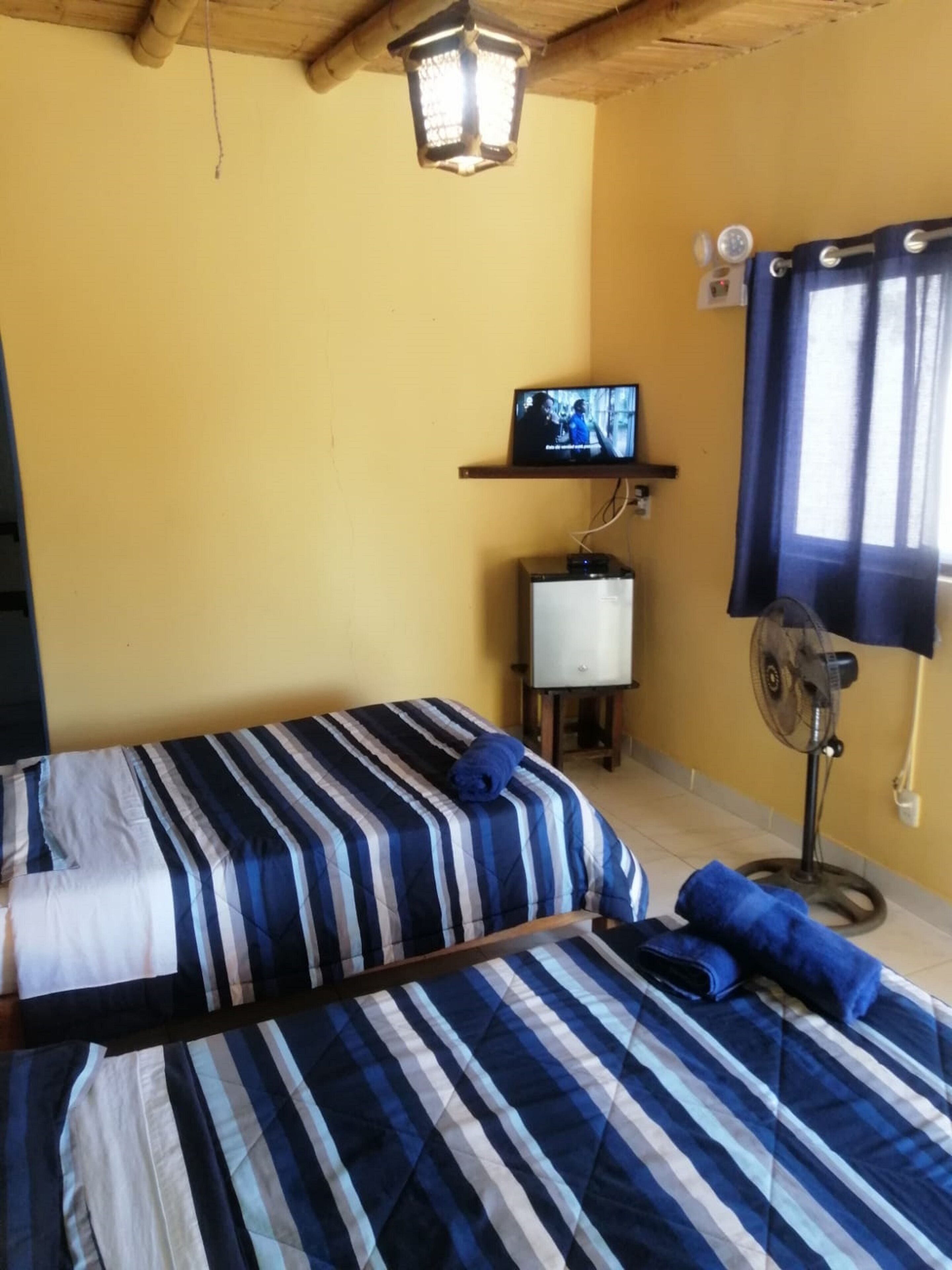 A room with two beds, a television, a fan, and a window with curtains.