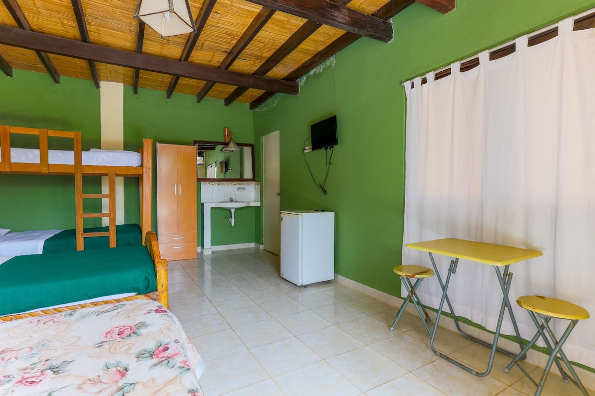 Una habitación con literas, una kitchenette pequeña, un escritorio y una mesa con sillas.