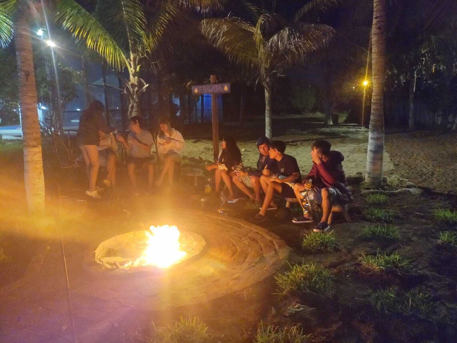 Un grupo de personas sentadas alrededor de una fogata por la noche en un entorno tropical con palmeras.