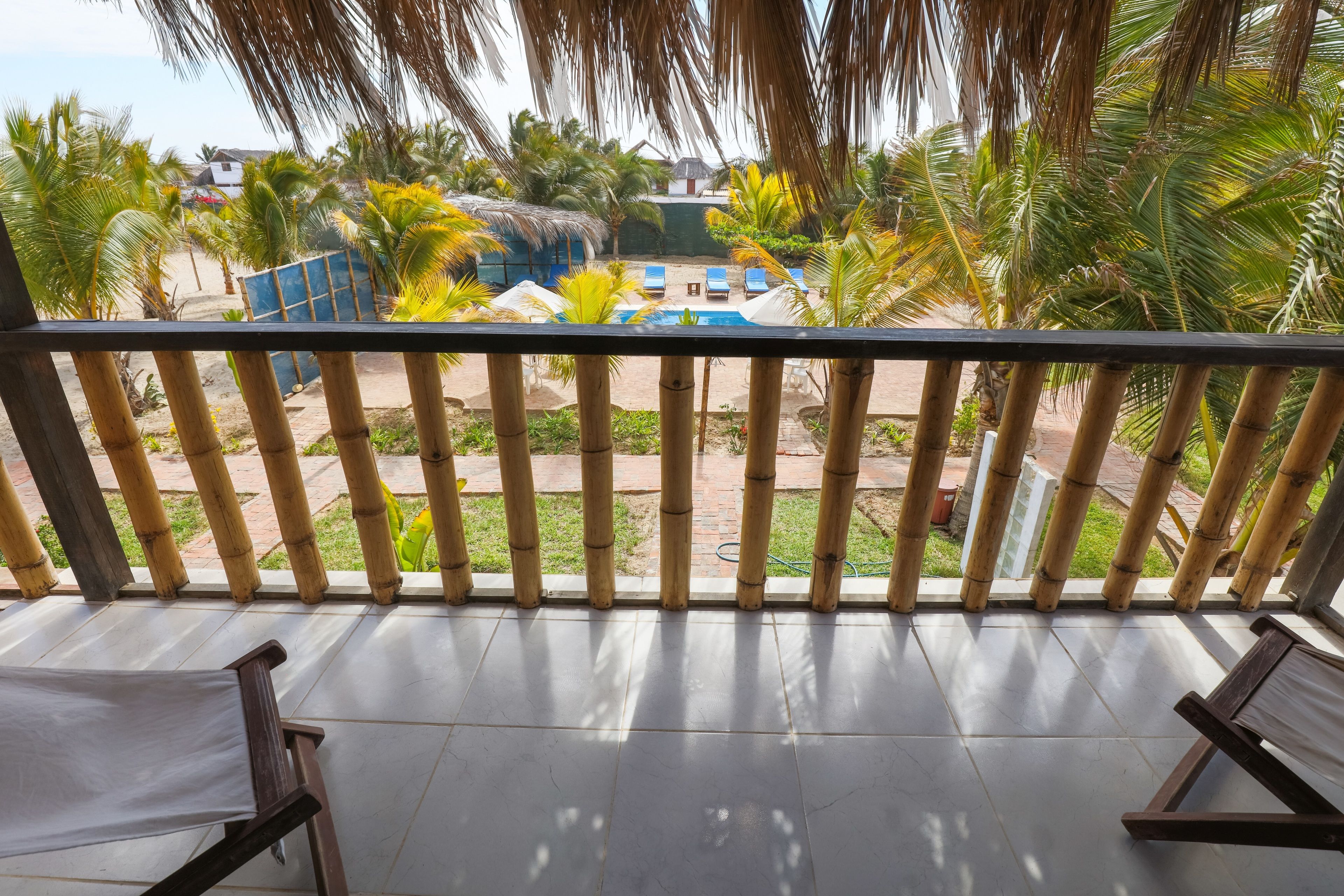Un balcón con vistas a una zona de piscina, que incluye sillas de descanso y palmeras.