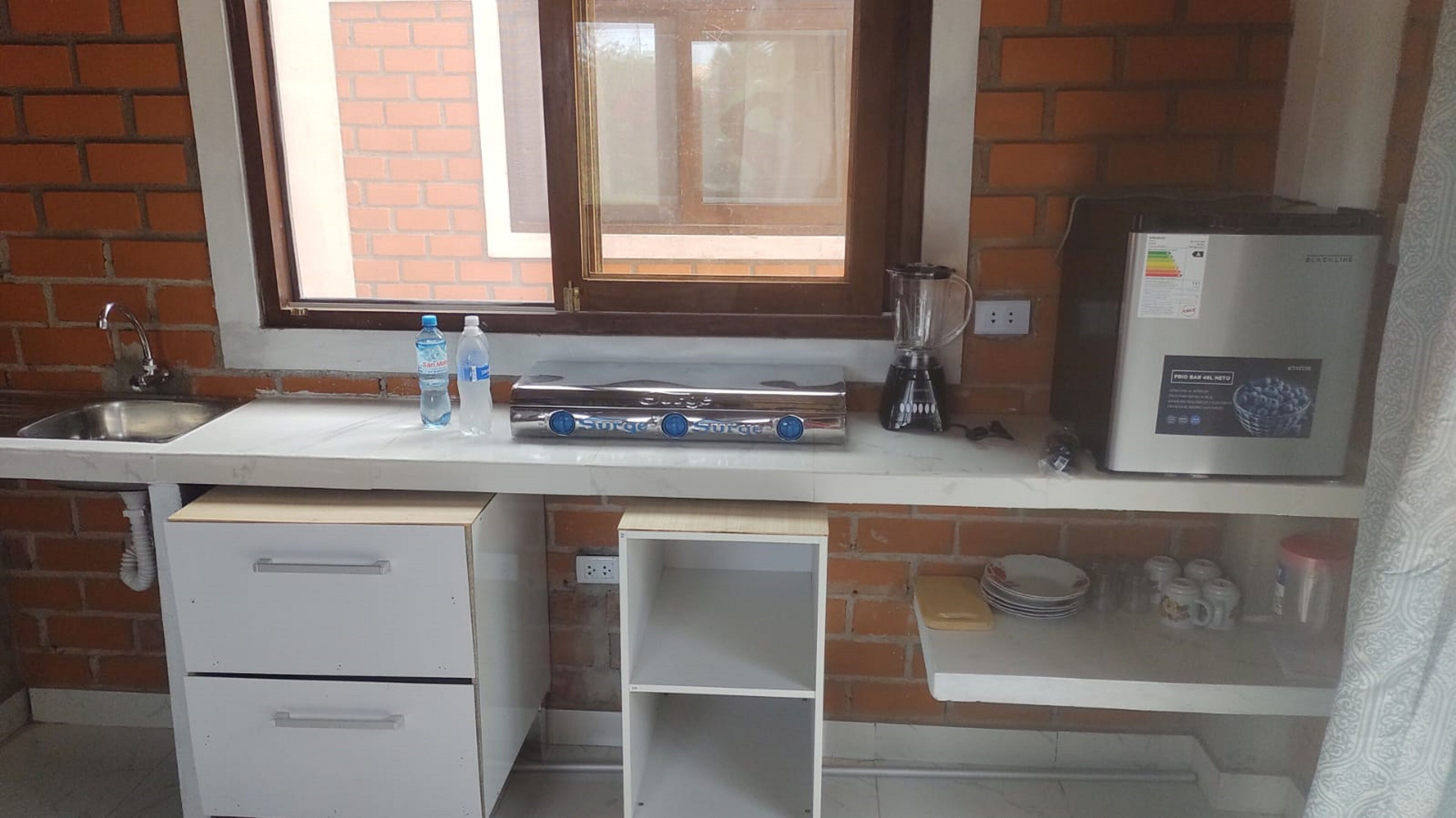 A kitchen with a sink, a window, a blender, a microwave, and a refrigerator.