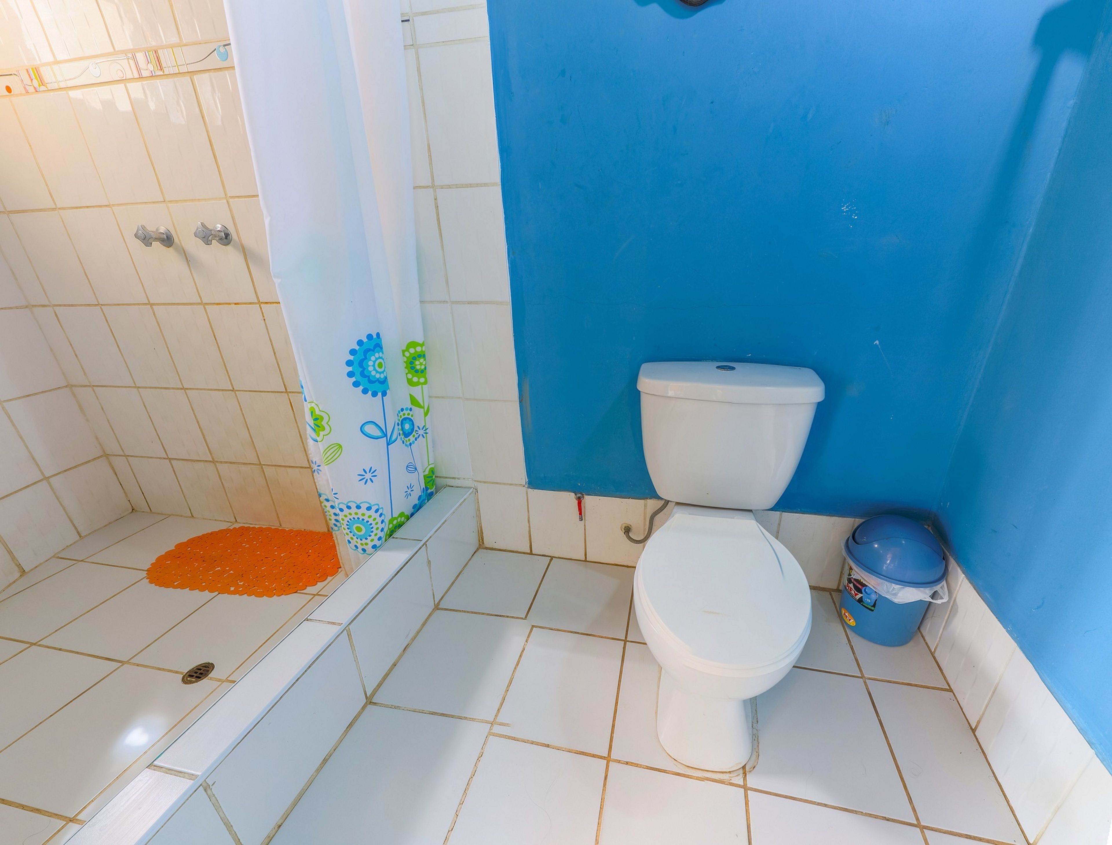 Een badkamer met een wit toilet, blauwe wanden en een douchegedeelte met een vloer van witte tegels.