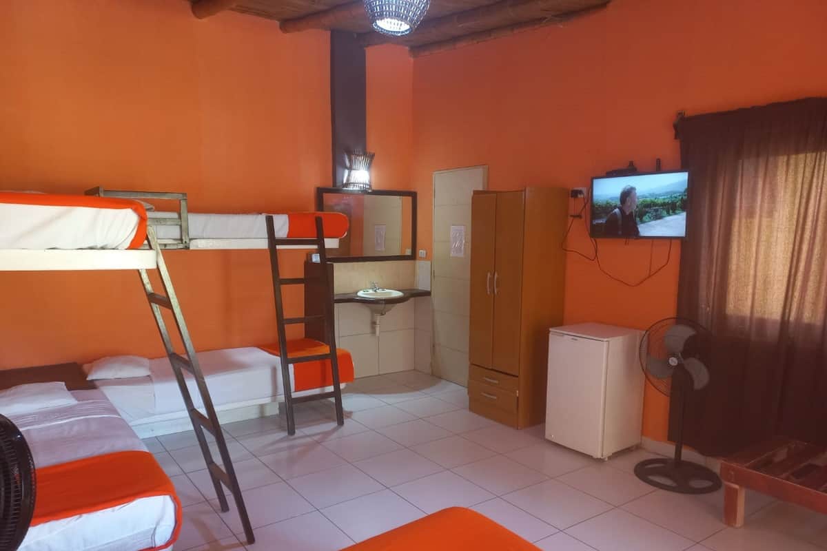 Habitación tipo dormitorio con literas, un escritorio, un armario pequeño, un televisor y un ventilador.