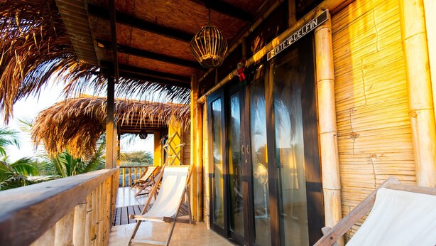 Una terraza de madera con sillas reclinables, techo de paja y una puerta de cristal con la inscripción "Suiten D'ELFIN".