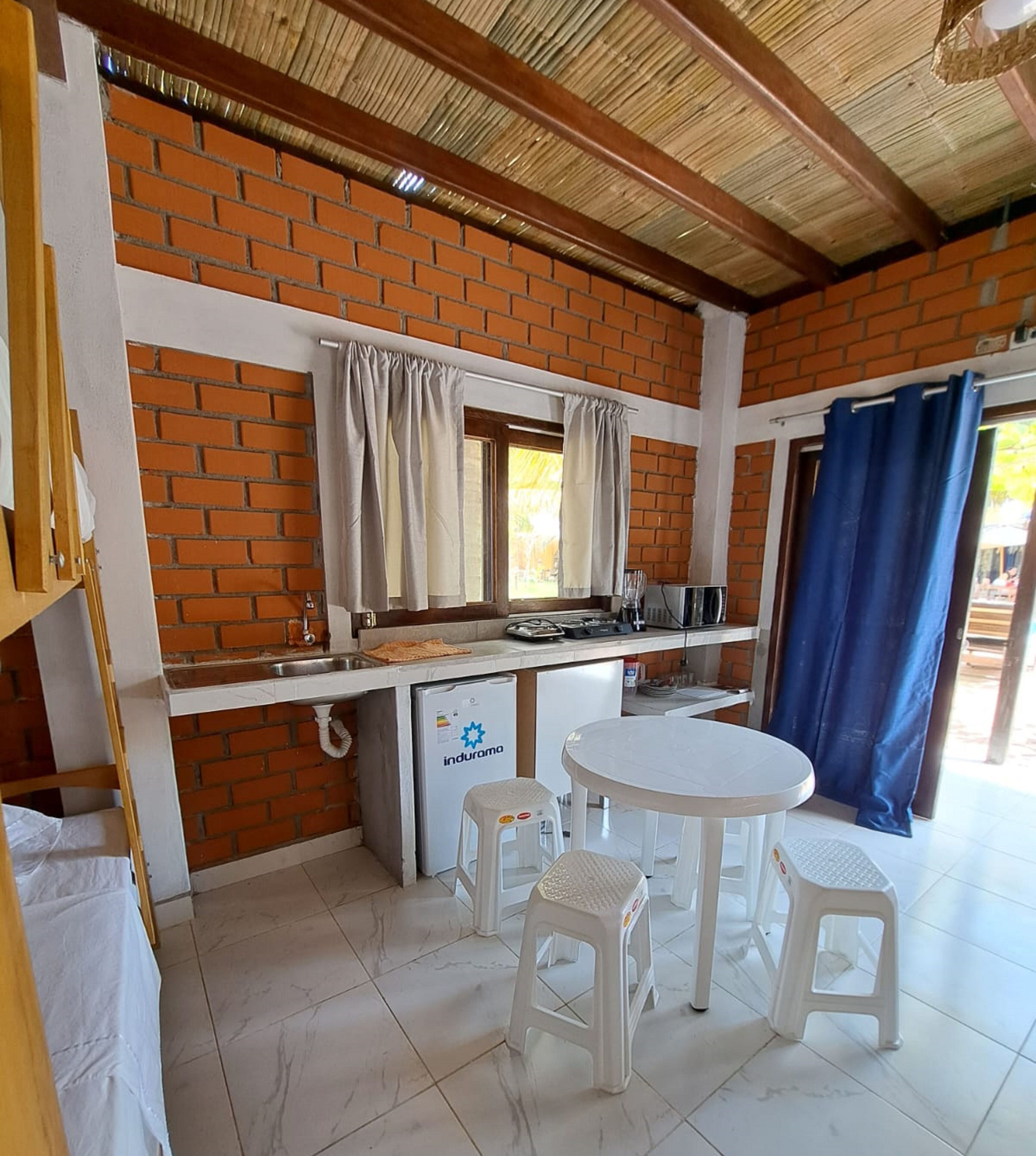 Una cocina compacta con pared de ladrillo, un refrigerador pequeño, un microondas y una mesa blanca con taburetes.