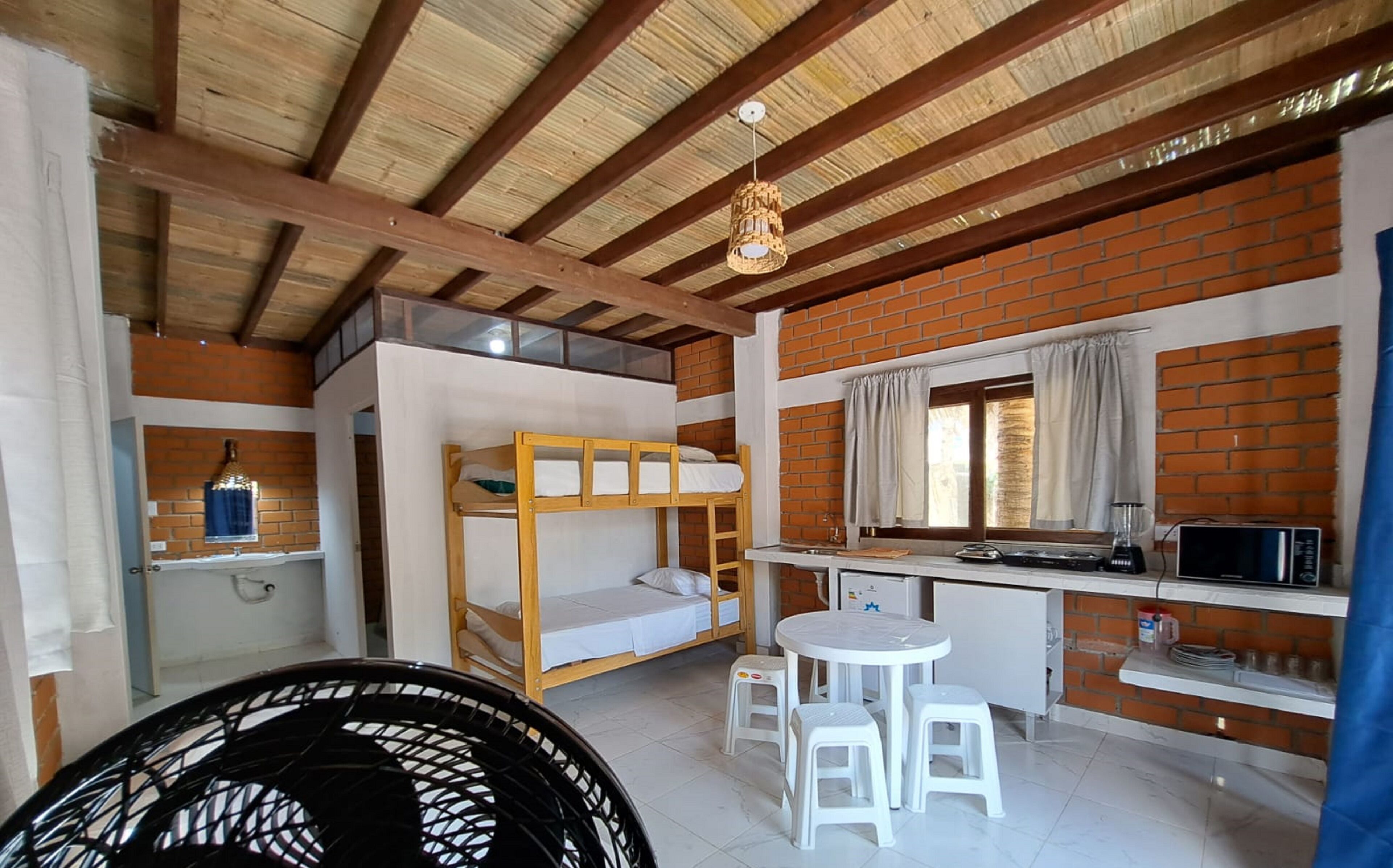 Una habitación compacta con literas, una kitchenette pequeña, una mesa de comedor con dos taburetes y una lámpara colgante.