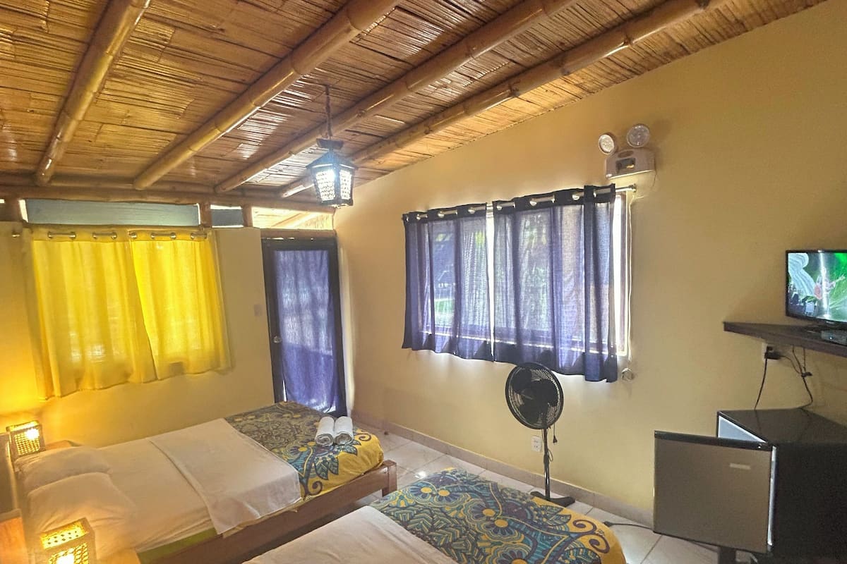 Una habitación con dos camas, un escritorio con computadora, un ventilador y un televisor.