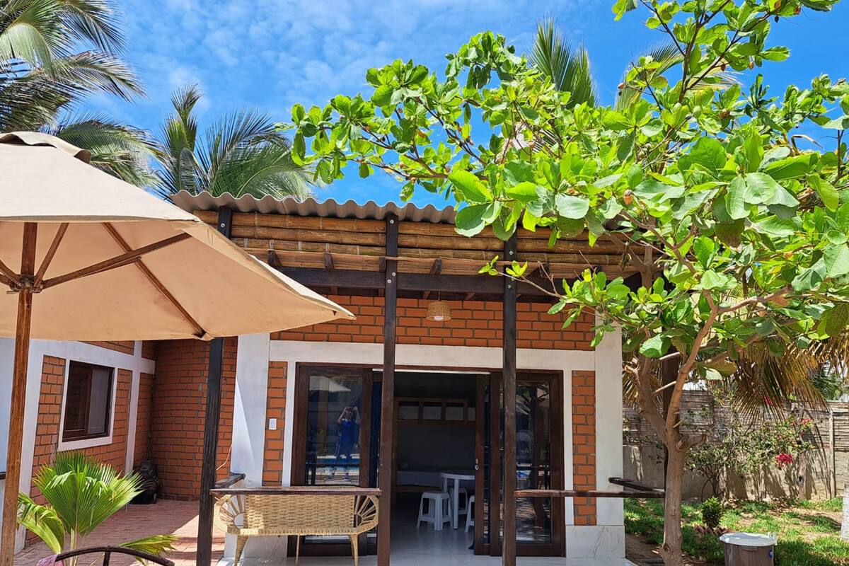 Un patio con una mesa y sillas, un paraguas grande y vista a un edificio de ladrillo con puertas de vidrio.