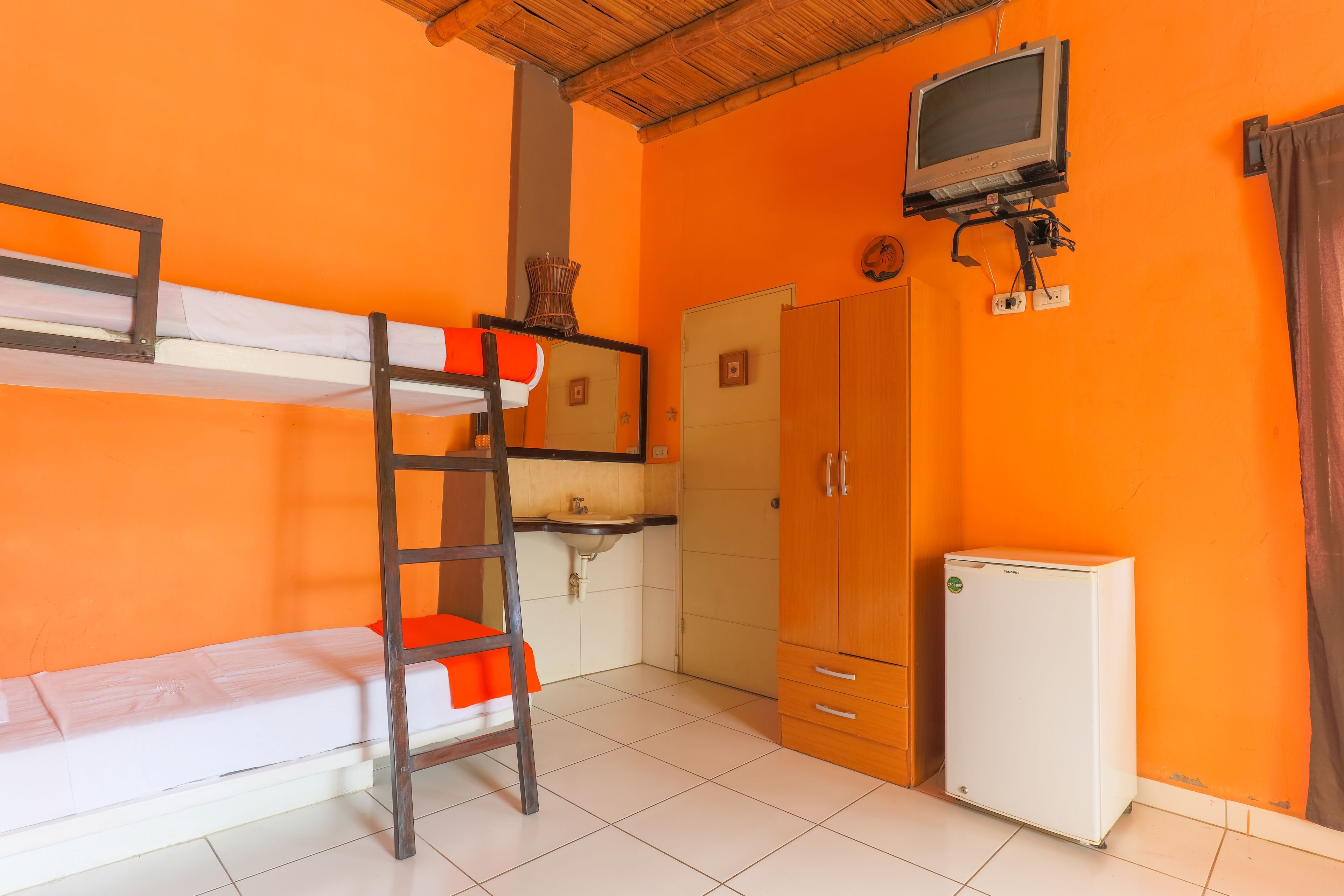 A room with bunk beds, a small sink, a wardrobe, a television, and a refrigerator.