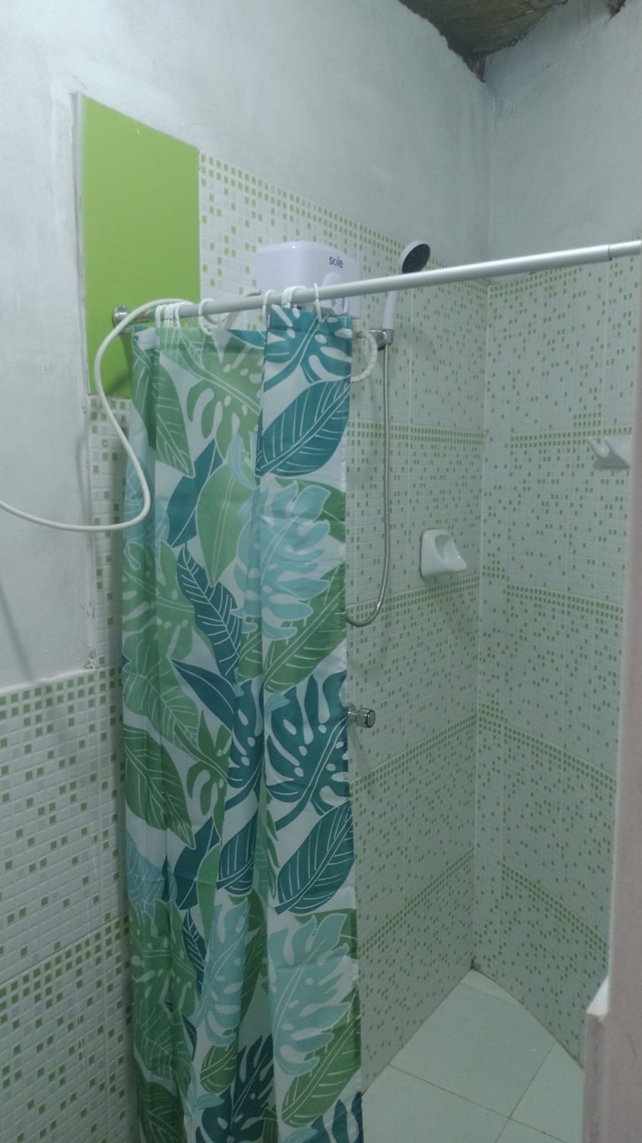 A shower area with a curtain featuring a leaf pattern, a handheld showerhead, and a wall-mounted control.