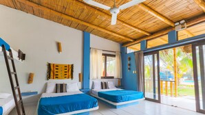 Una habitación con dos camas, ventilador de techo y ventanas amplias.