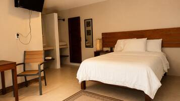 Habitación de hotel con una cama, un escritorio, una silla, un televisor montado en la pared y una mesita de noche con una lámpara.