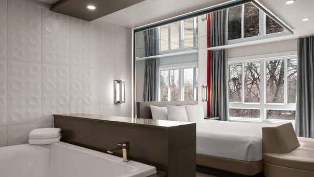 A modern bedroom with a large window, a bathtub, and a sofa. - Ramada by Wyndham Laval (Laval)
