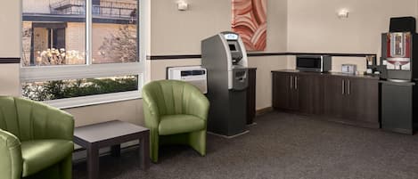 A hotel room with a window, a green chair, a small table, an ATM, a microwave, and a coffee machine.