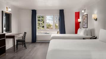 A hotel room with a desk, two beds, a chair, a window with curtains, and wall-mounted lights.