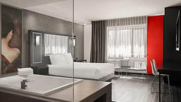 A modern hotel room with a large bed, a separate seating area, a large mirror, and a bathtub.