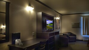 A hotel room with a flat-screen TV mounted on the wall, a small table with chairs, a desk, and a window with blinds. - Ramada by Wyndham Laval (Laval)