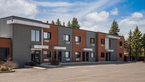 A modern multi-story building with a parking lot in front. - Ramada by Wyndham Laval (Laval)