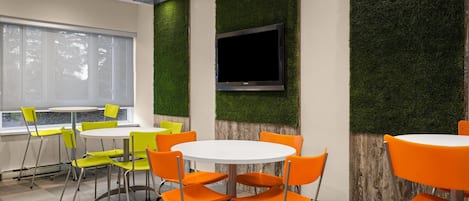 Habitación moderna con una mesa redonda, sillas naranjas, un televisor de pantalla plana y detalles decorativos en la pared en color verde.