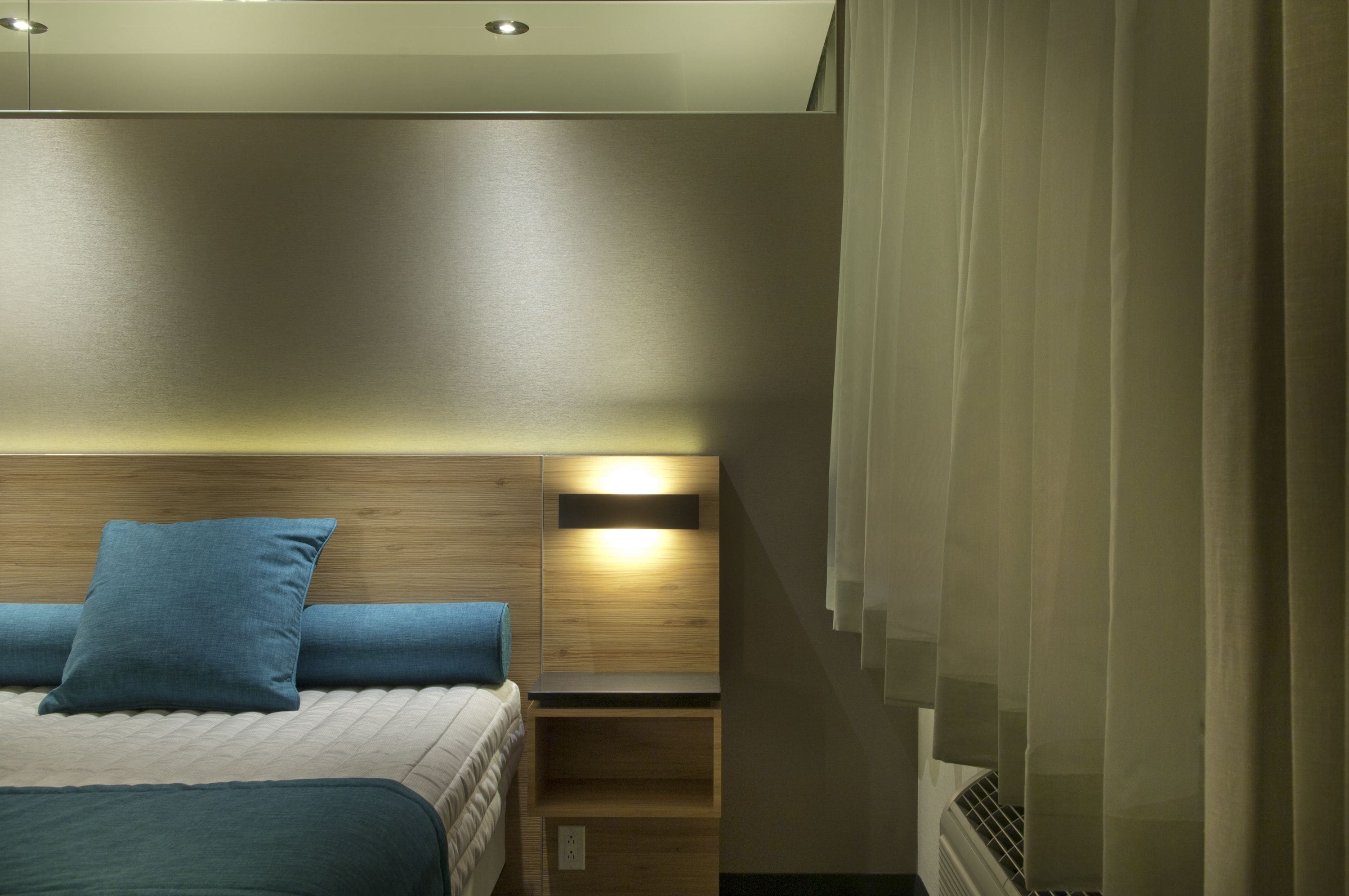 Una habitación de hotel moderna con una cama, una mesita de noche, un estante en la pared y un ventanal con cortinas.