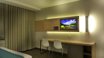 Une chambre d’hôtel comprenant un lit, un bureau avec deux chaises, un téléviseur fixé au mur et une fenêtre avec des rideaux.
