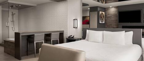 Una habitación de hotel moderna con una cama grande, un escritorio con dos sillas, ducha y televisión.