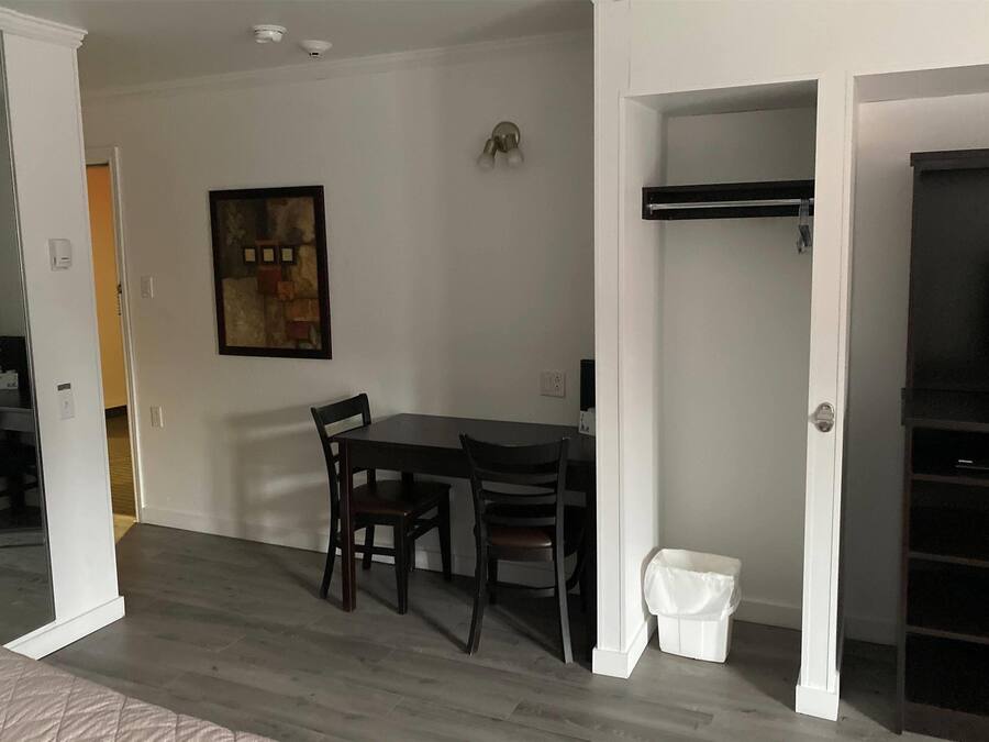 A room with a dining table and chairs, a small white trash bin, and a painting on the wall.