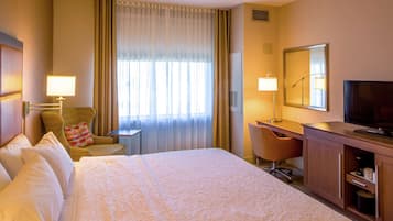 Une chambre d’hôtel avec un grand lit, un bureau avec une chaise, une télévision et une fenêtre avec des rideaux.