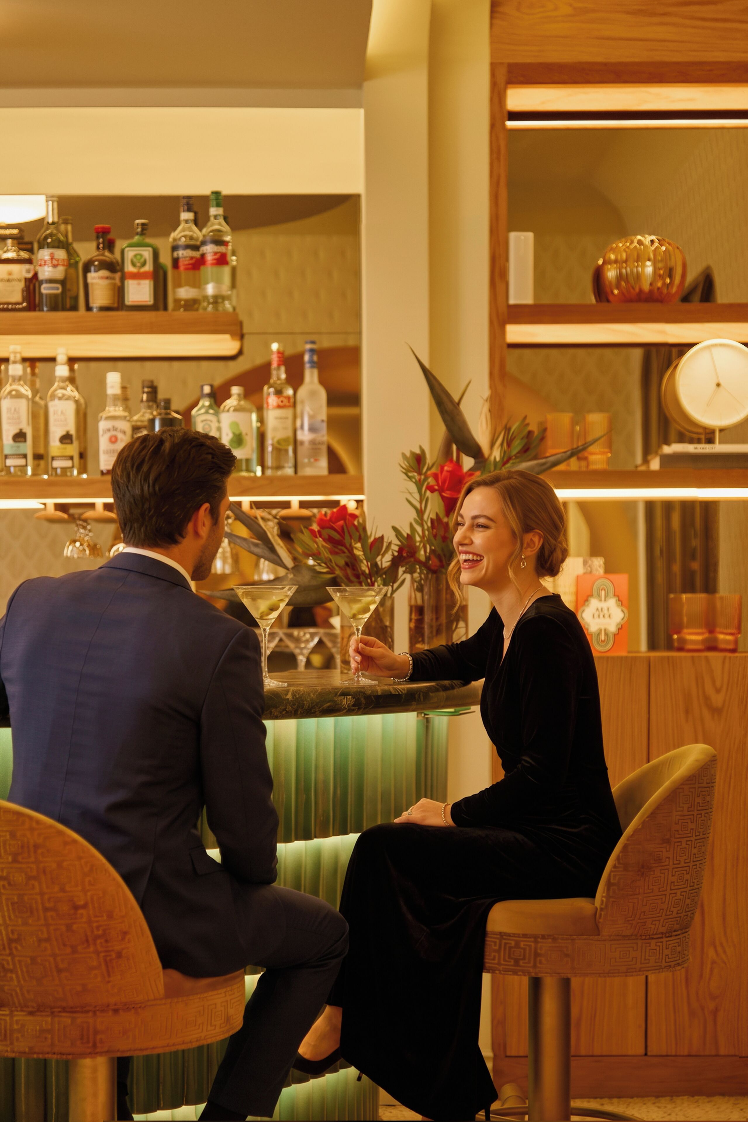 Een bar met een toog, planken met flessen en een klok aan de muur.