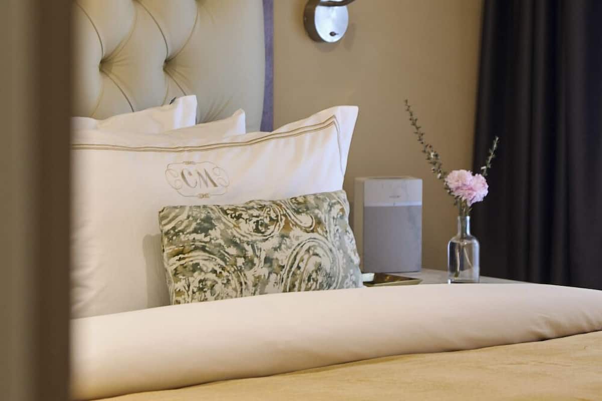 A neatly made bed with a tufted headboard, a bedside table with a vase of flowers, and a wall-mounted lamp.