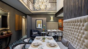A dining area with a high ceiling, a chandelier, and a tufted headboard.