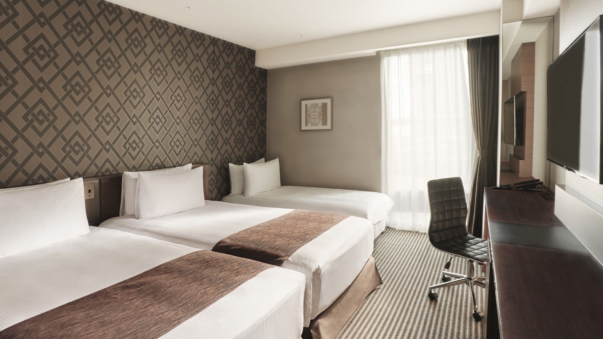 Une chambre d’hôtel avec deux lits, un bureau, une chaise, une télévision et un papier peint à motifs.